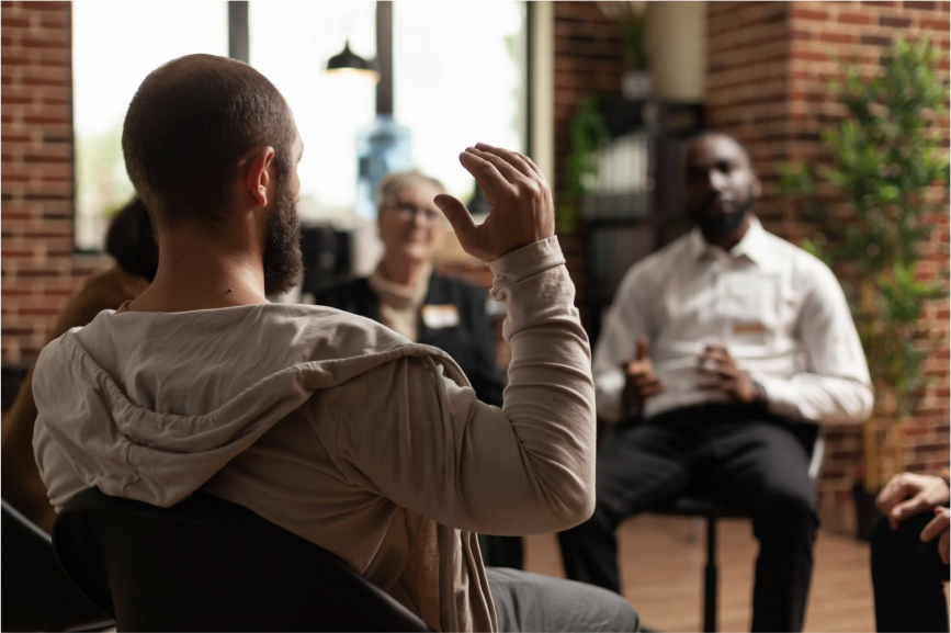 Autistic adult discussing his challenges and experiences in front of professionals in a supportive setting.