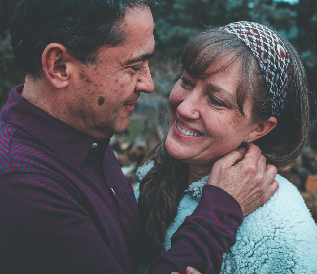 A neurodiverse couple is looking into each other's eyes while facing each other. The man's hand rests on his wife's shoulder.
